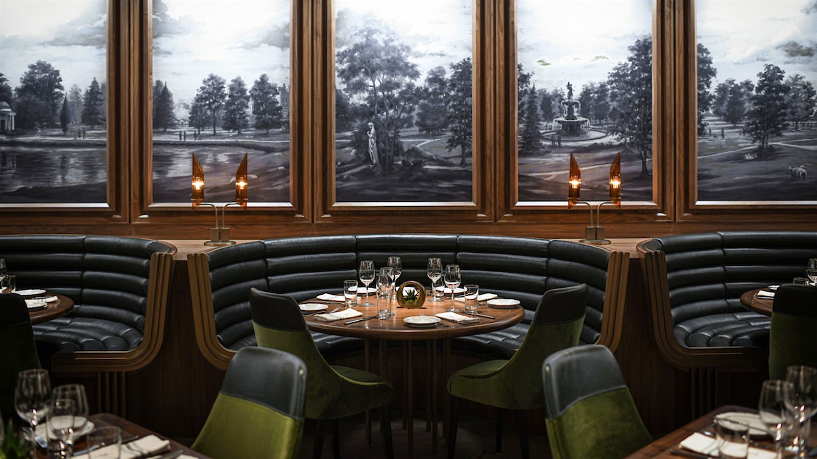 Dark gray booths at set wood tables at Reign, with murals of outdoor scenes on the wall